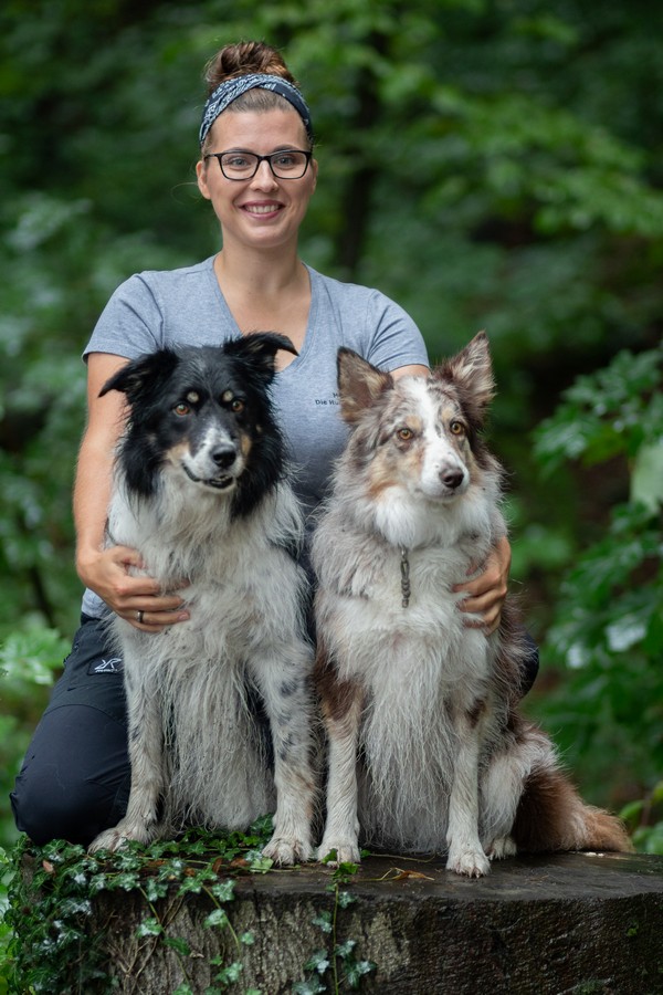 Hundelehrerin_Maria Kurz Maria Kurz steht hinter ihren beiden Border Collie Hündinnen Cathy und Dörte. Alle schauen in die Kamera
